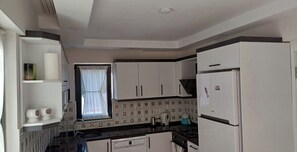 Une cuisine de taille réduite, avec des meubles blancs, une cuisinière à gaz et un réfrigérateur.
