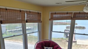 A room with large windows overlooking a body of water, a red chair with a cushion, and a small round table.