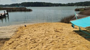 A sandy beach with footprints, a hammock, and a boat in the background.