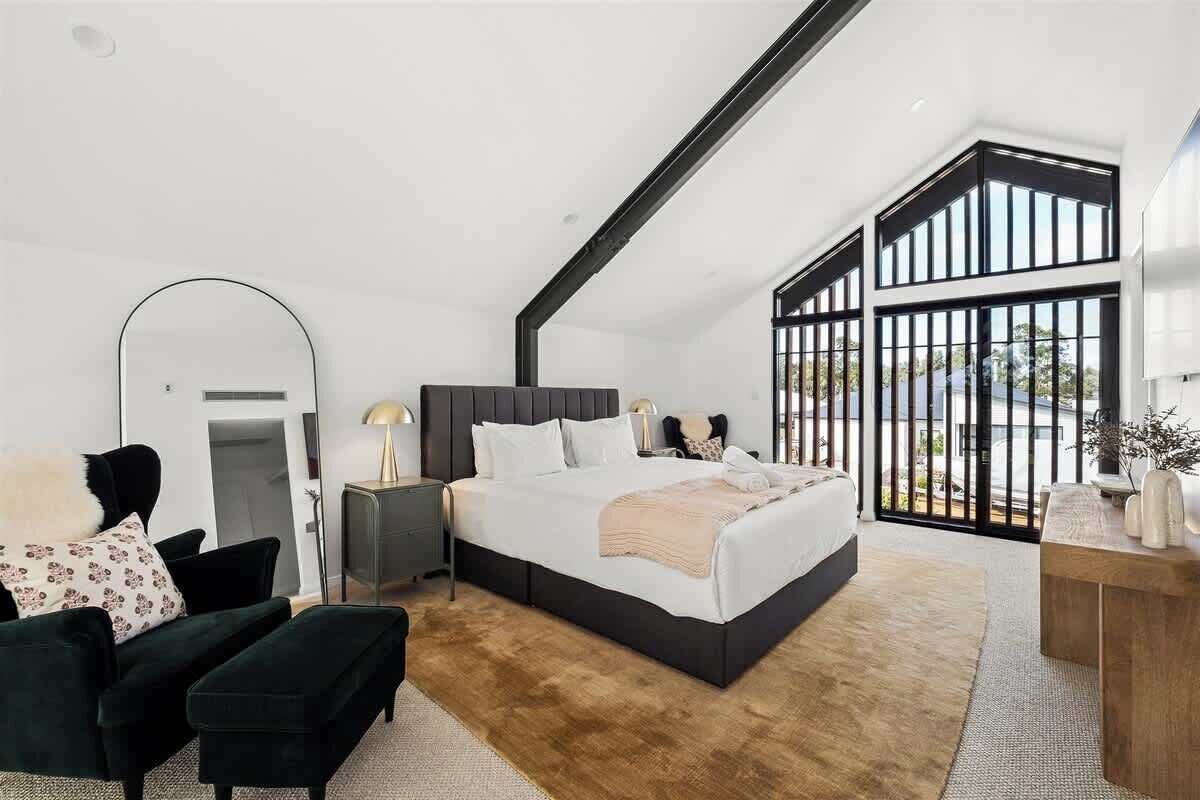 Un dormitorio moderno con una cama grande, un cabecero oscuro, una mesita de noche de madera y vistas a través de un ventanal.