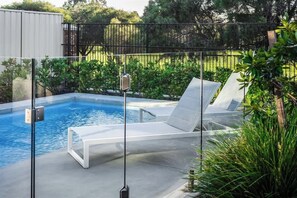 Une piscine entourée de parois en verre, une chaise longue et une clôture en métal.