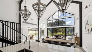 A modern kitchen with a central island, large windows, and hanging pendant lights. - Ember & Aqua—Luxury Barnhouse on the Golf Course (Dunsborough)