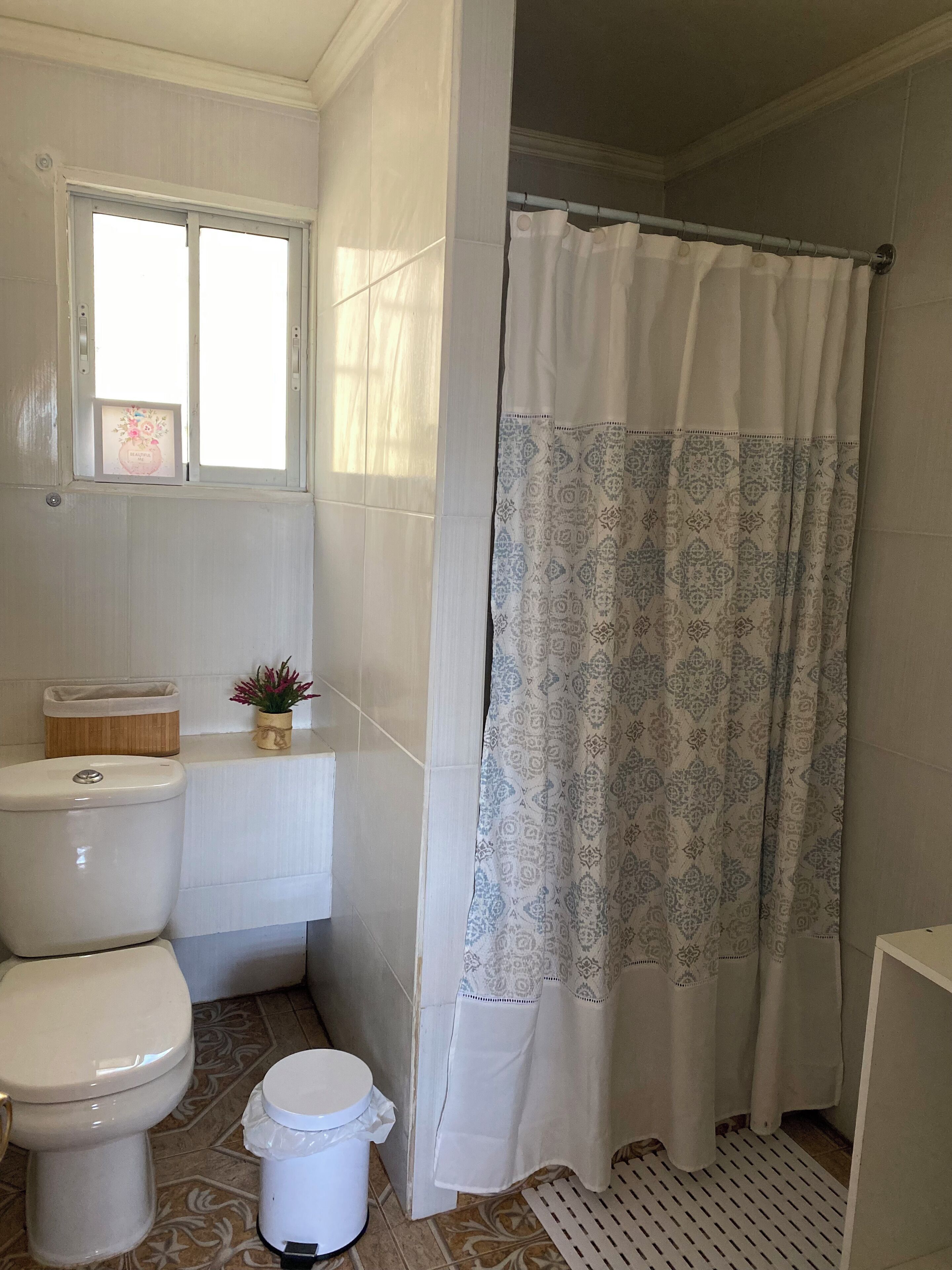 Une salle de bain avec des toilettes, un petit lavabo, un rideau de douche et une fenêtre.