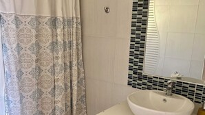 Ein Badezimmer mit einem gemusterten Duschvorhang, einem weißen Waschbecken und einem Spiegel darüber sowie einem gemusterten Boden.