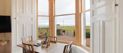 A dining area with a bay window, wooden table, chairs, and a view of the outdoors.