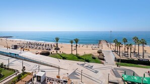 A beachside promenade with palm trees, a sandy beach, and a clear view of the ocean. - 'Paraná' Apartment with Balcony, Wi-Fi, and Air Conditioning (Quarteira)