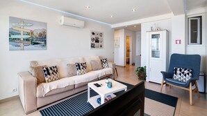 A living room with a sofa, armchair, coffee table, and artwork on the wall. - 'Paraná' Apartment with Balcony, Wi-Fi, and Air Conditioning (Quarteira)