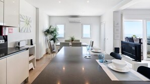A modern kitchen with a central island, a dining area with a table and chairs, and a view through a large window. - 'Paraná' Apartment with Balcony, Wi-Fi, and Air Conditioning (Quarteira)