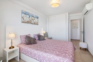 Une chambre à coucher comprenant un lit, des lampes de chevet, une table de chevet, un petit tabouret et une porte donnant sur une autre pièce.