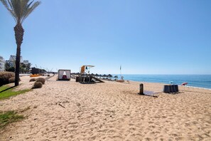 Une plage avec un palmier, des parasols et une tour de surveillance pour les sauveteurs.