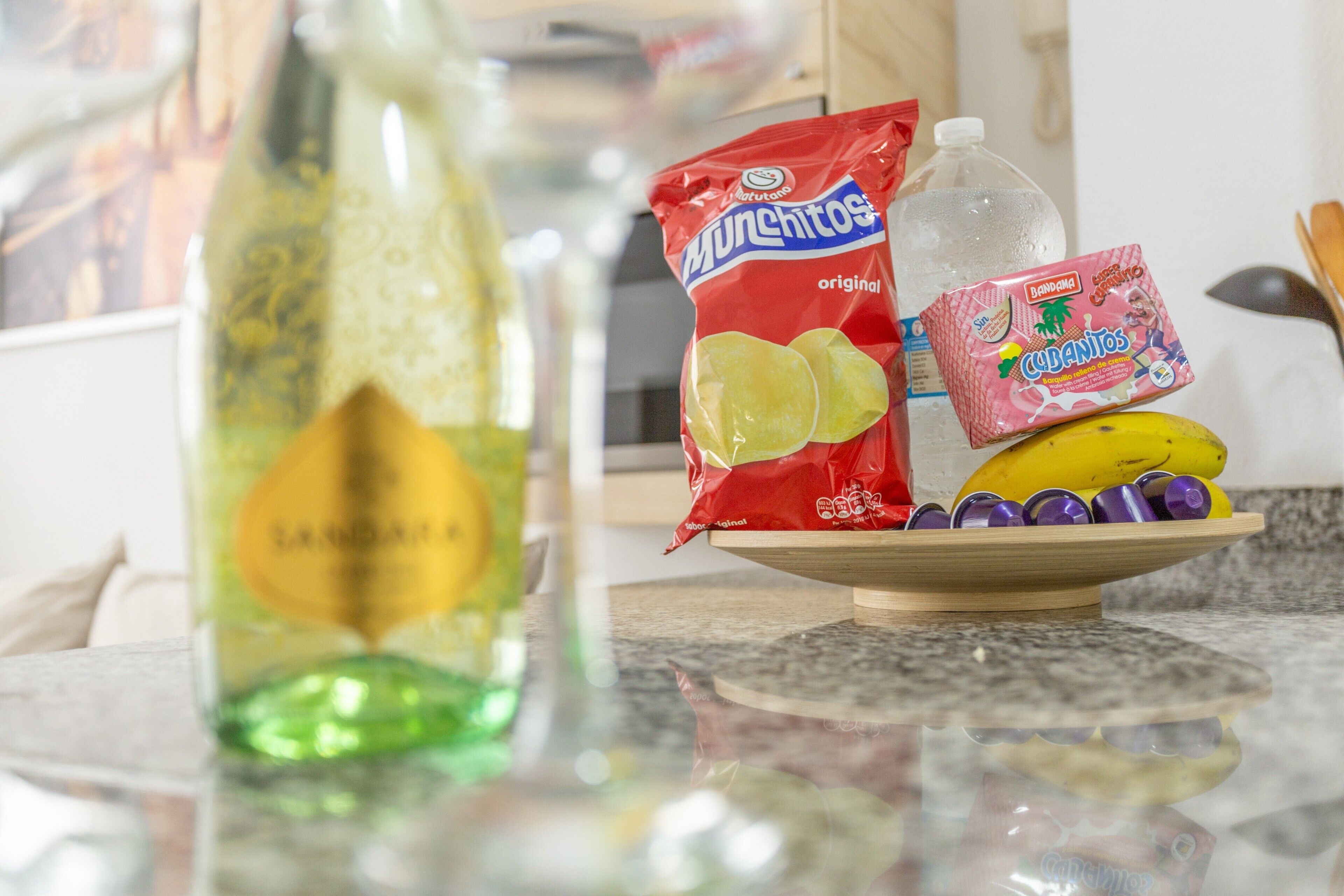 A kitchen counter with a bottle, a bag of chips, a banana, and a packet of Cubantos.