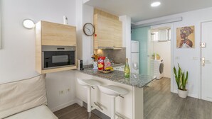 Een moderne keuken met een magnetron, spoelbak en barstoelen. Er hangt een klok aan de muur en er staat een potplant.