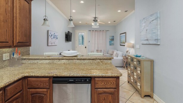 A kitchen with granite countertops, wooden cabinets, a dishwasher, pendant lights, and a dining area with a white table and chairs. - 2 Bed 2 Bath 2nd Fl Condo by Beach with Pool (South Padre Island)