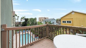 A balcony with a wooden railing overlooking a swimming pool and a yellow building. - 2 Bed 2 Bath 2nd Fl Condo by Beach with Pool (South Padre Island)