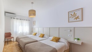 Hotelkamer met twee bedden, een stoel, een hanglamp, een wandplank met een plant en een lijst met kunstwerk.