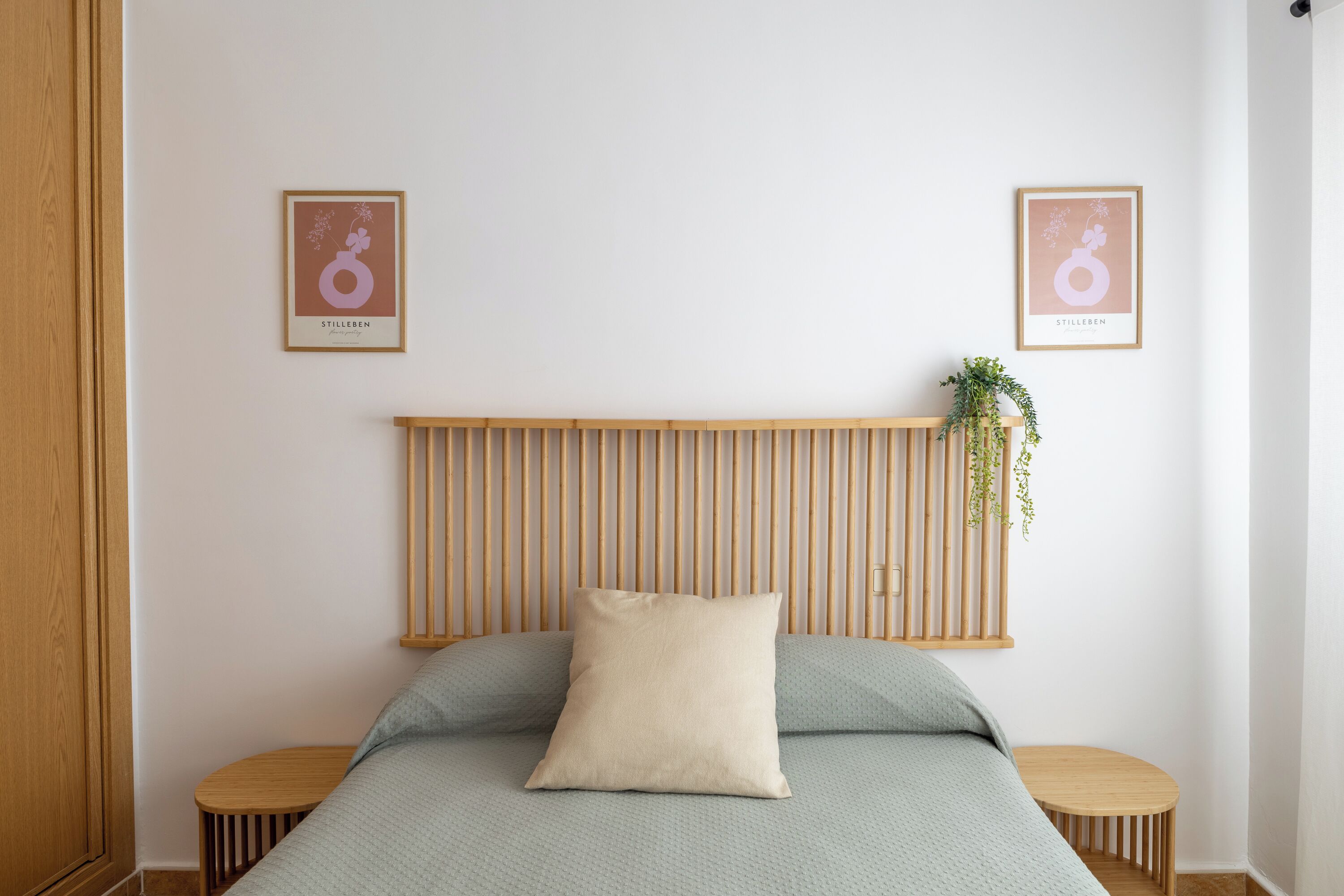 A bedroom with a bed, two bedside tables, a wooden headboard, and two framed pictures on the wall.