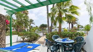 Une terrasse avec des chaises longues, une table et une pergola.