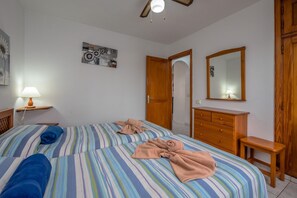 Une chambre avec deux lits, une commode en bois, un miroir et un ventilateur de plafond.