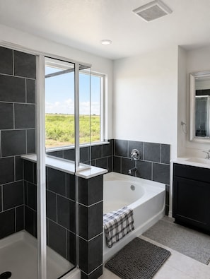 A modern bathroom with a bathtub, a glass shower enclosure, and a view of the outdoors.
