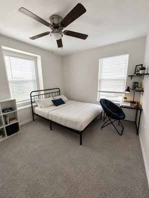 A bedroom with a bed, a desk, a chair, a ceiling fan, and a bookshelf. - Light and Airy 4-bedroom home in New Braunfels (New Braunfels)
