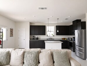 Une cuisine moderne avec des meubles de couleur sombre, un réfrigérateur en acier inoxydable et un îlot central.