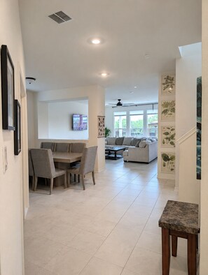 A spacious living area with a dining table, sofas, and a ceiling fan.
