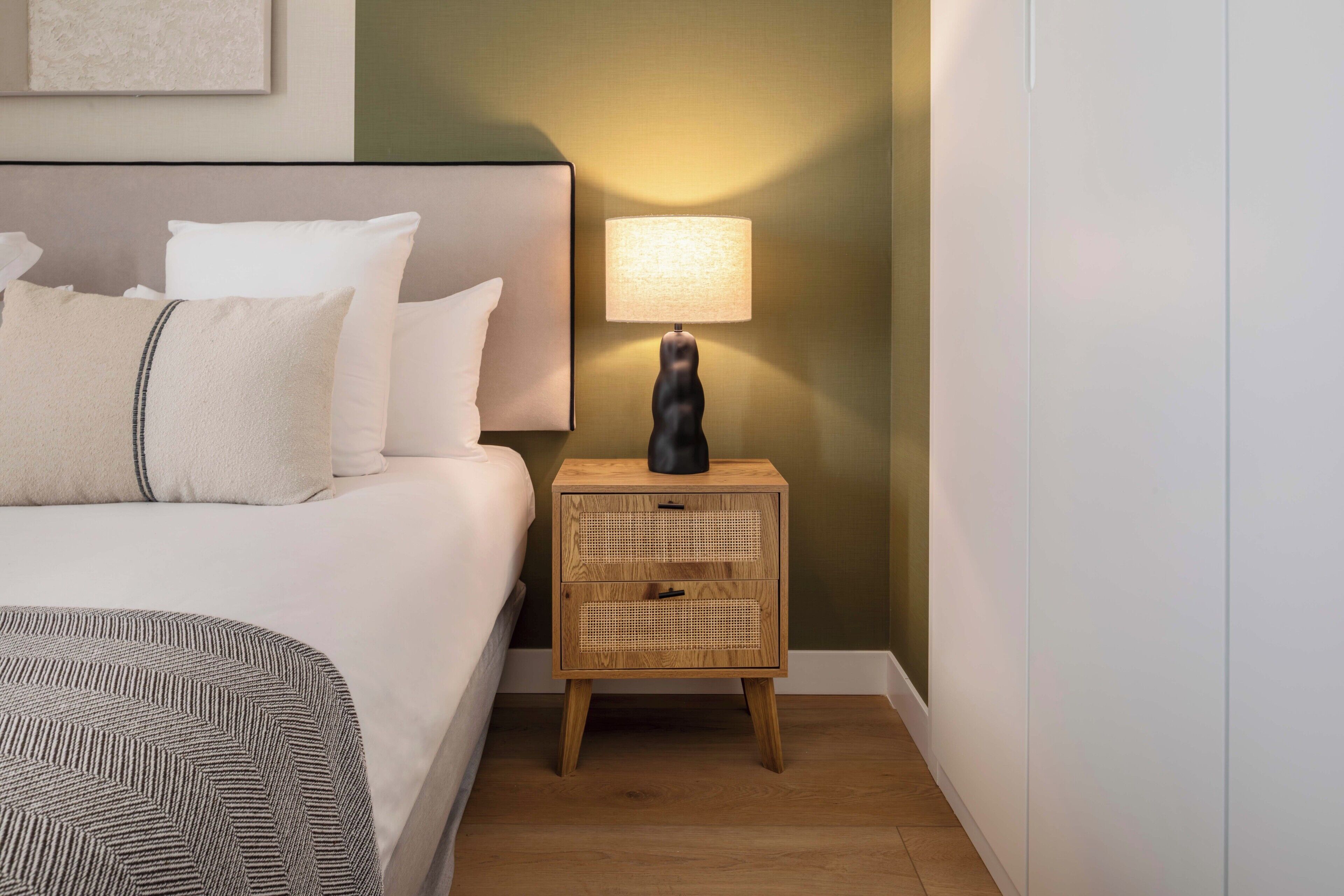 A neatly made bed with pillows and a bedside lamp on a wooden nightstand.