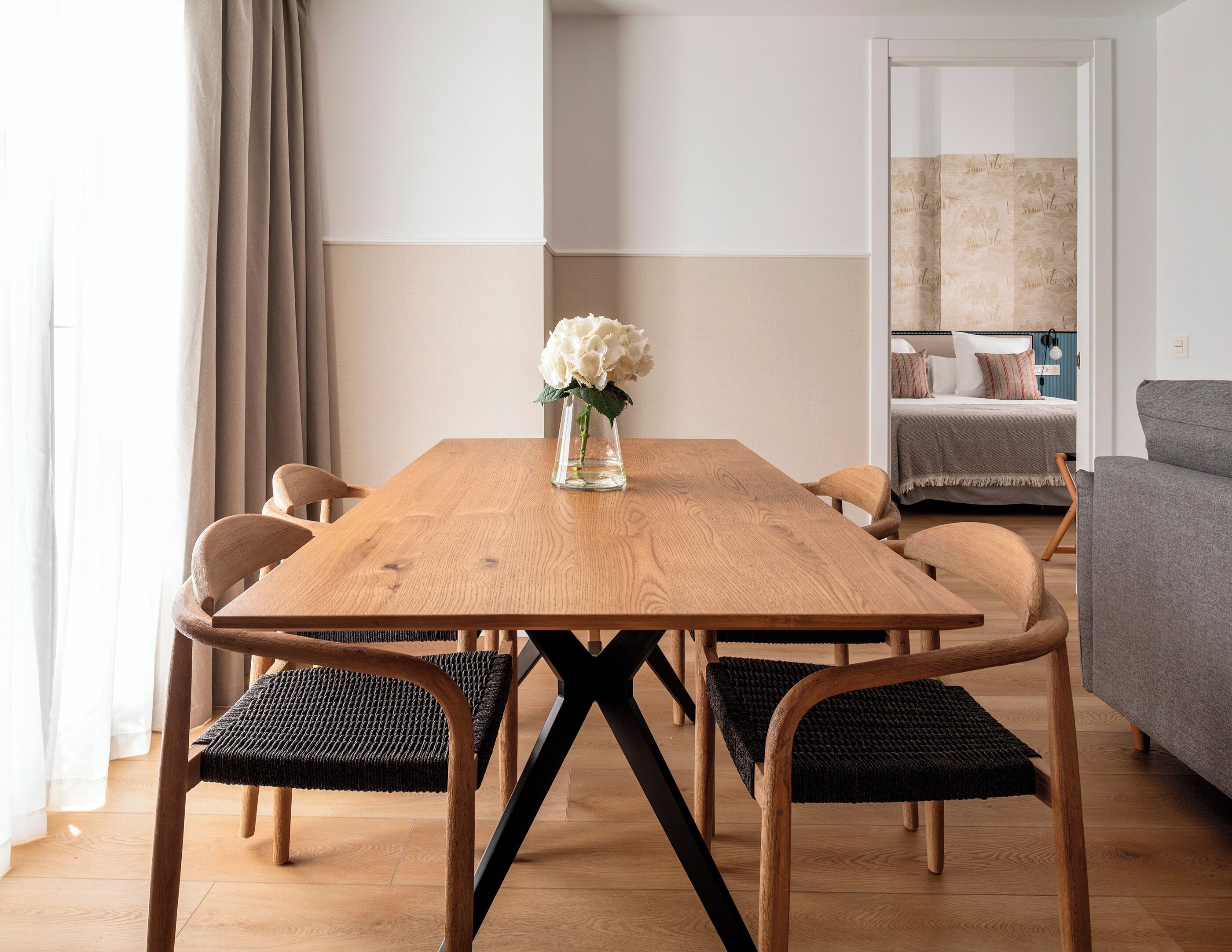 Ein Essbereich mit einem Holztisch, schwarzen gewebten Stühlen und einer Vase mit Blumen.