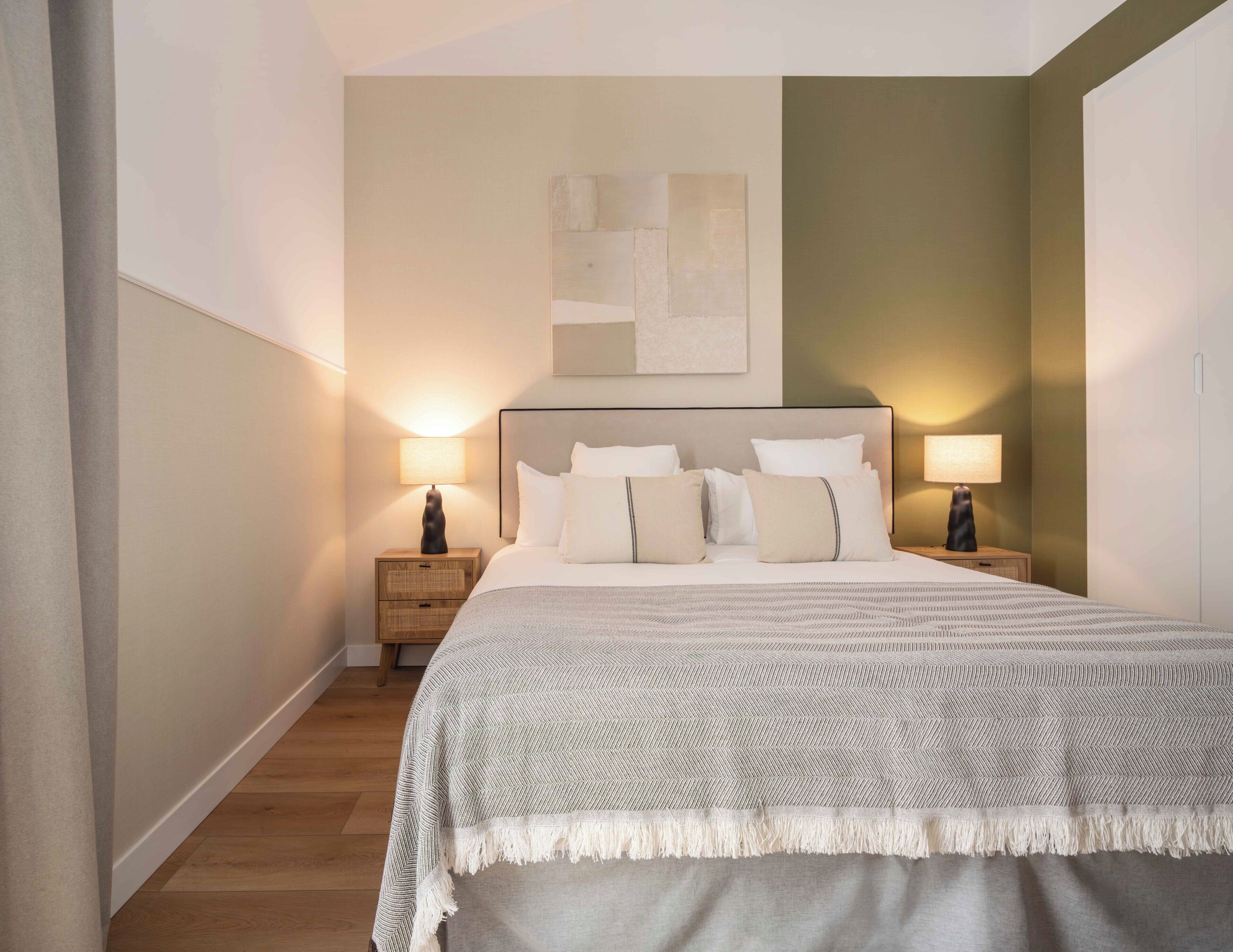A hotel room with a large bed, two bedside tables with lamps, a headboard, and a wall-mounted artwork.
