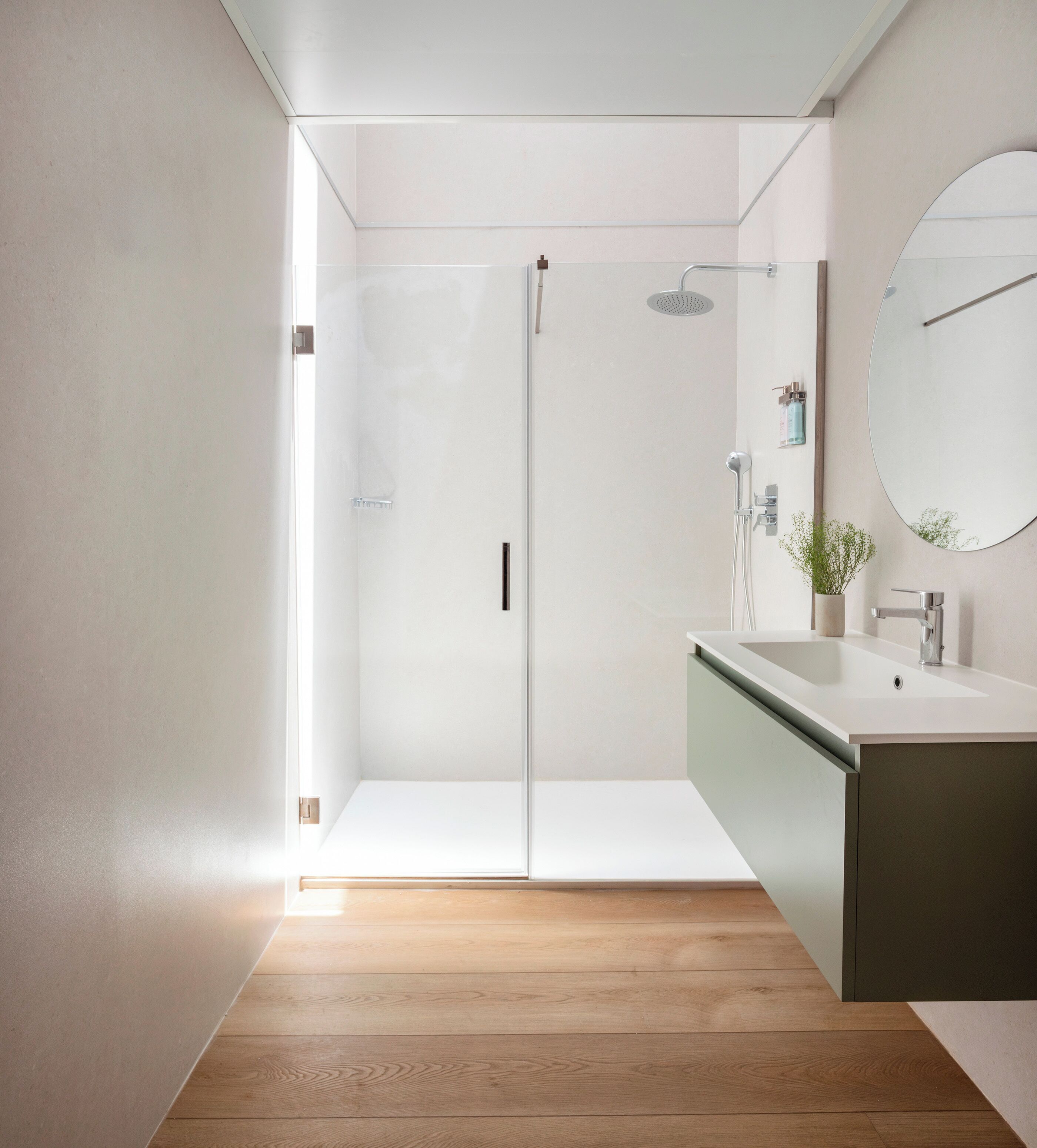 A modern bathroom with a glass shower enclosure, a sink with a mirror, and a wooden floor.