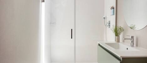 A modern bathroom with a glass shower enclosure, a sink with a mirror, and a wooden floor.