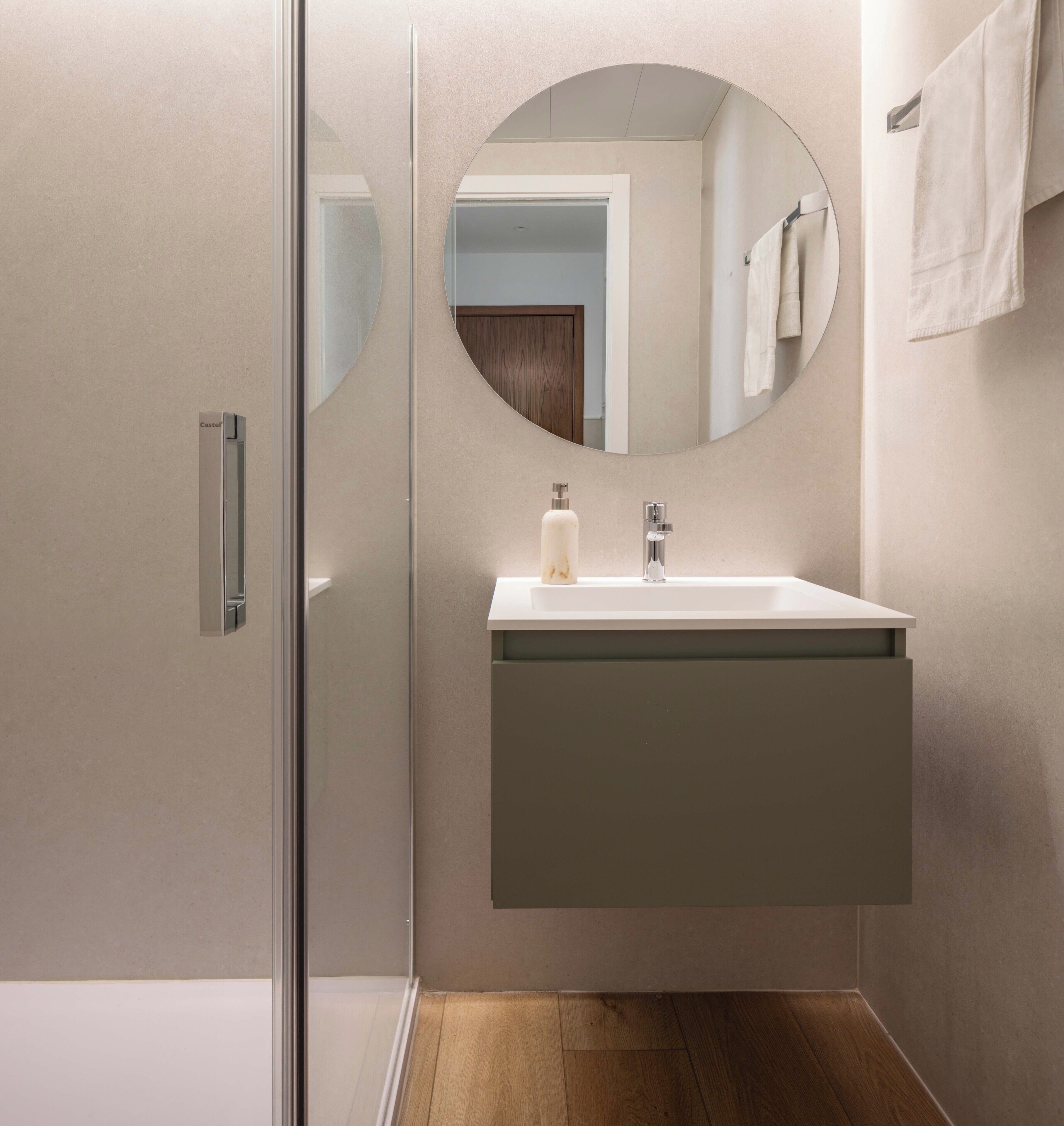 A modern bathroom with a glass shower enclosure, a white sink with a mirror above it, and a wooden floor.