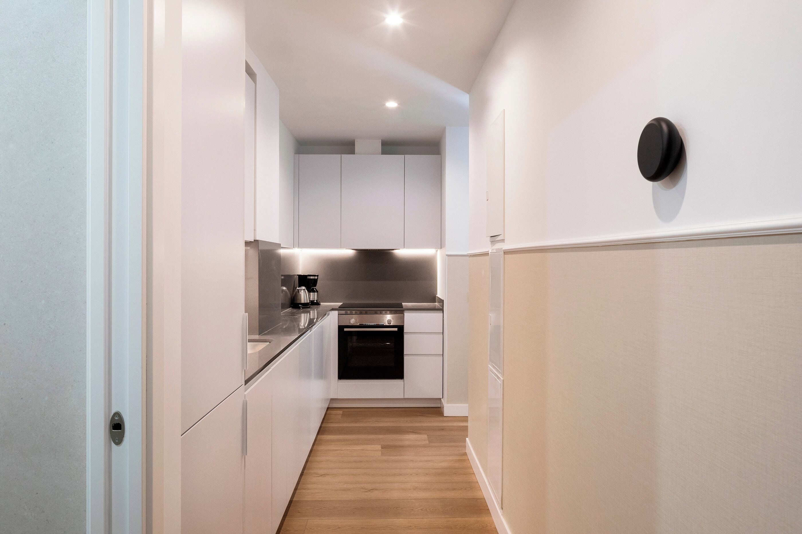 A narrow hallway leading to a kitchen with white cabinets, a stainless steel range, and a coffee maker.