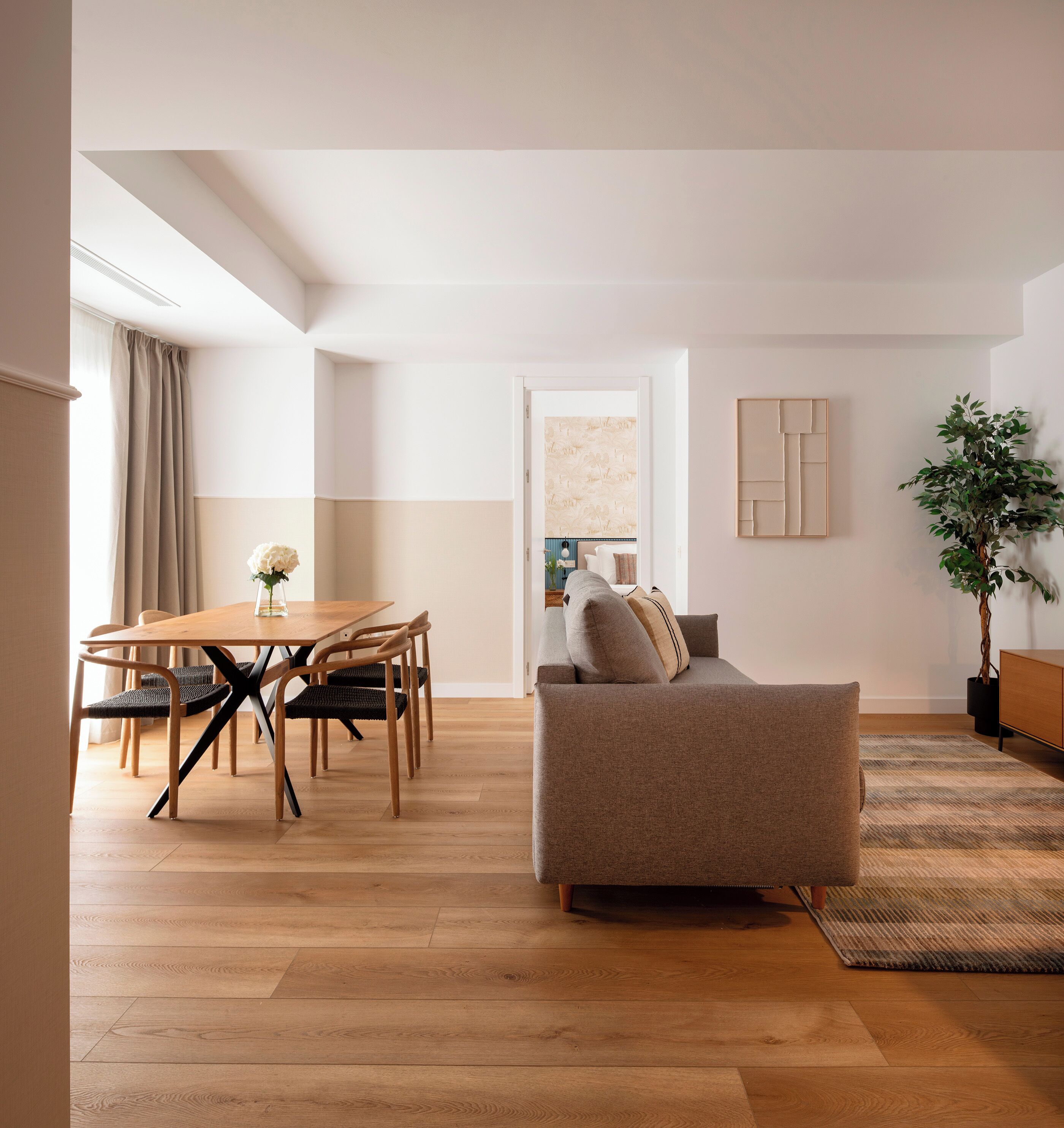 A modern living room with a wooden dining table, a sofa, and a potted plant.