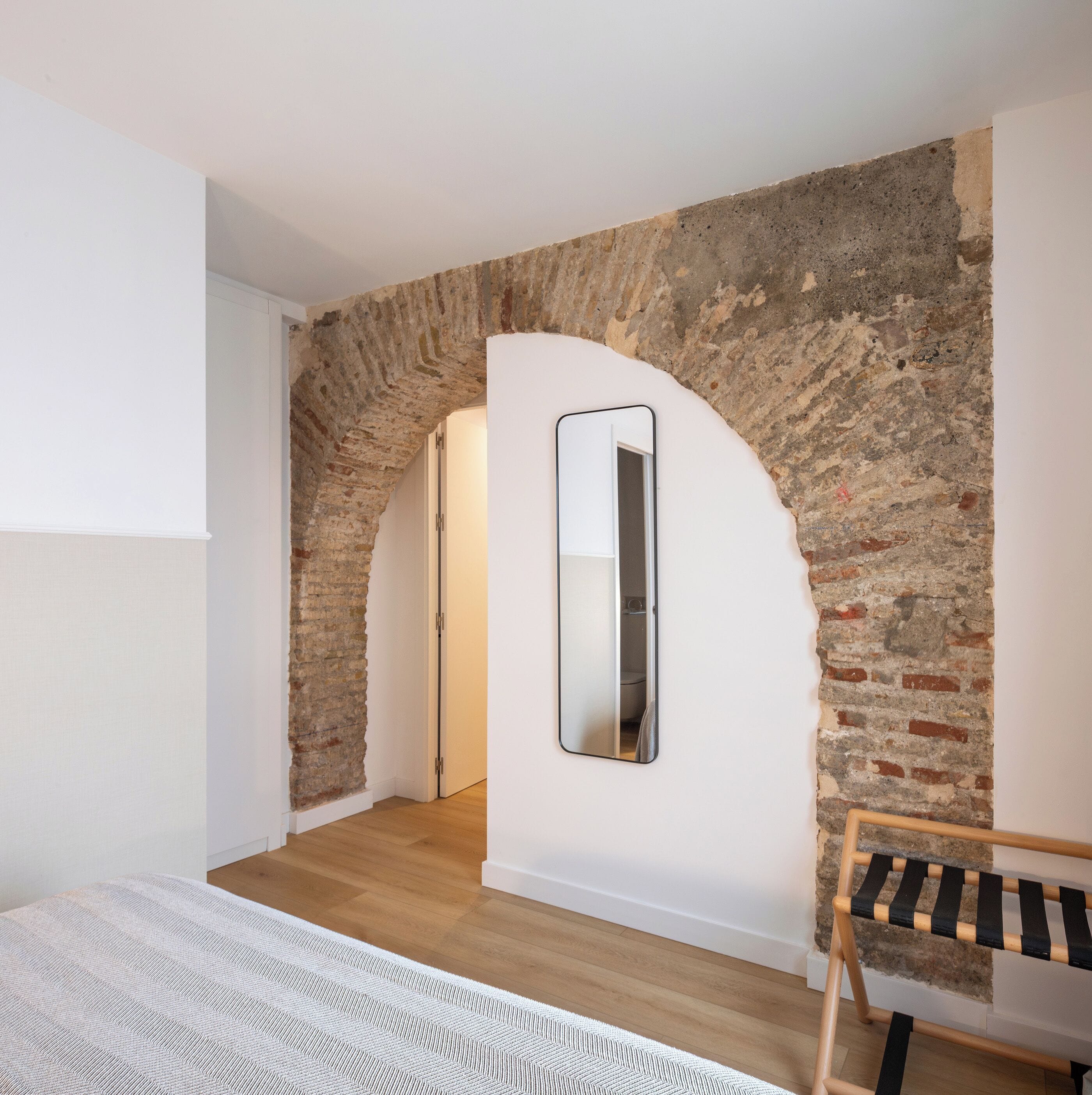 Una habitación con pared de ladrillo, suelo de madera, puerta blanca y un espejo.