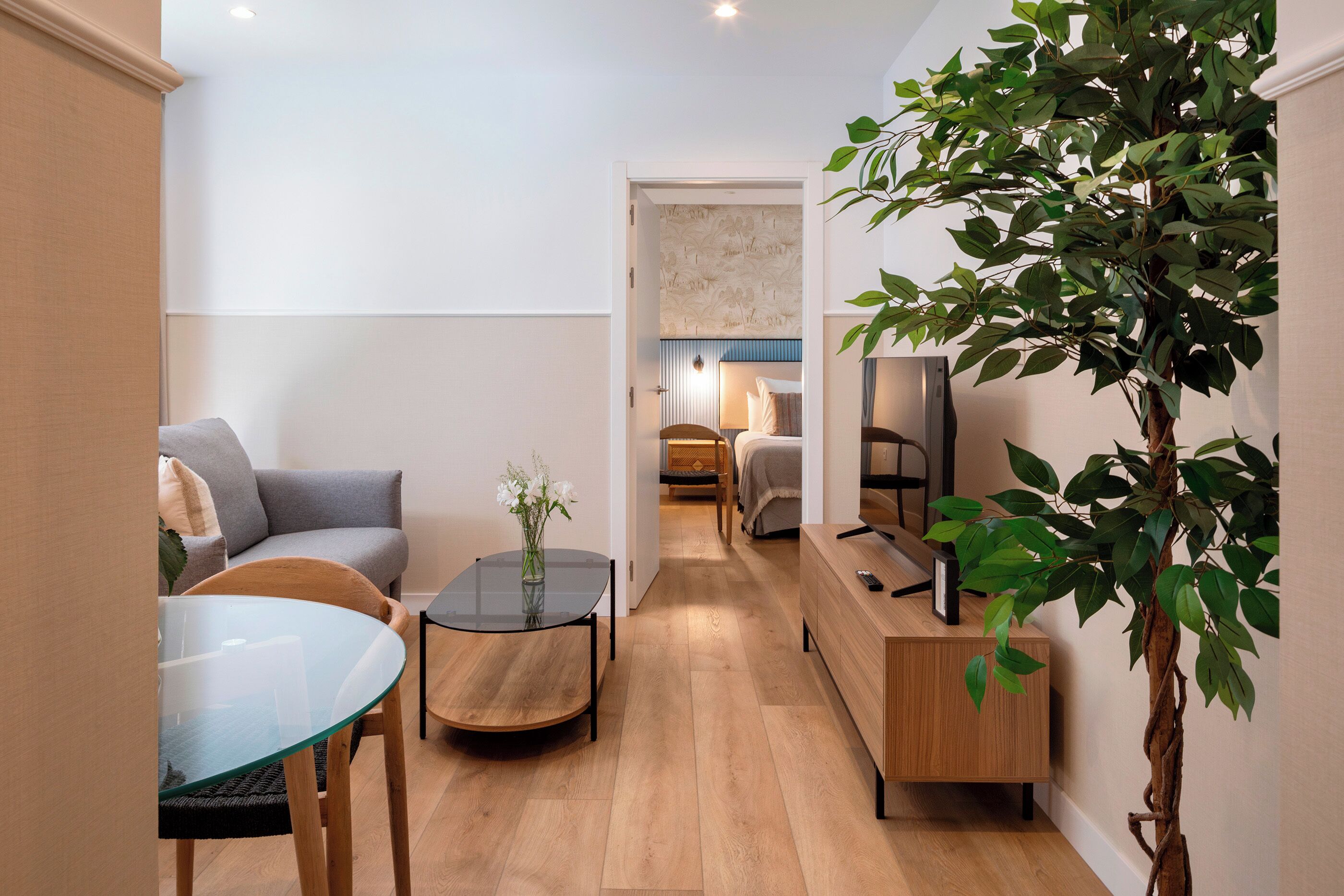 Una sala de estar moderna con un sofá, una mesa de centro de vidrio y un televisor sobre un mueble de madera.