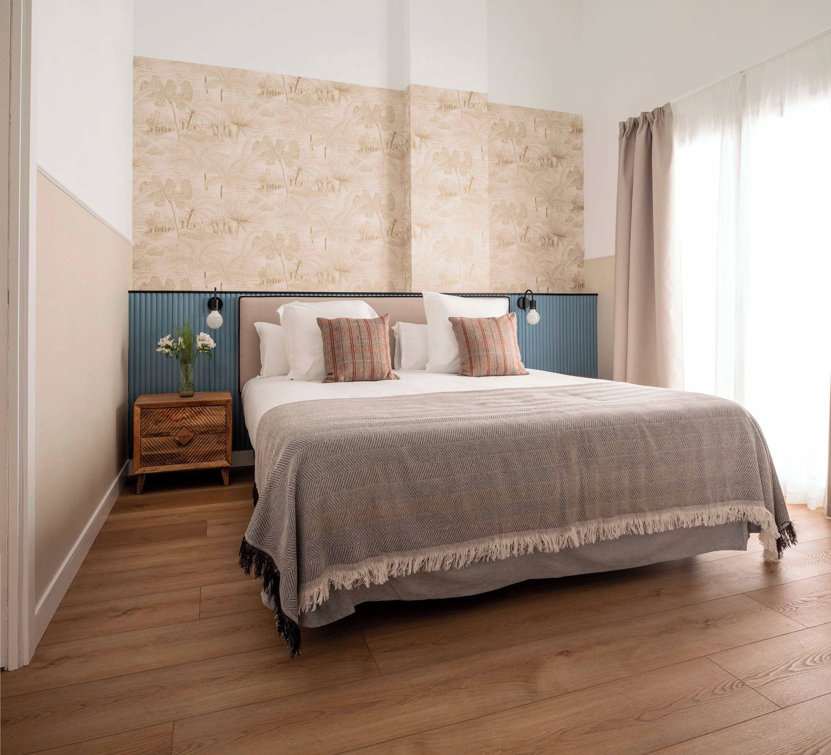 A bedroom with a large bed, a nightstand with a vase, and a wall with a textured pattern.