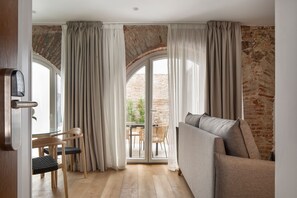 Une pièce comprenant un canapé, une table à manger avec des chaises, et donnant sur un espace extérieur grâce à une porte vitrée, cet espace étant bordé d’un mur en briques.