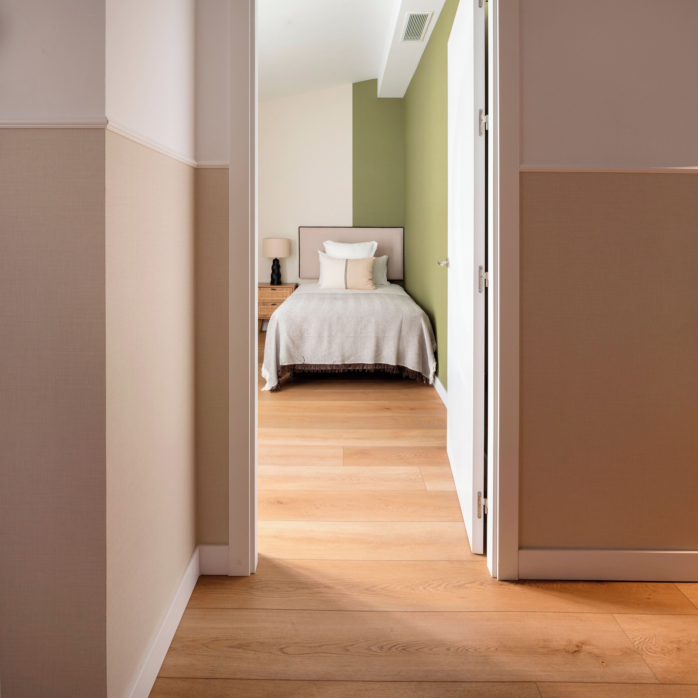 Une chambre d’hôtel avec un lit, une table de chevet, une lampe et une vue sur le couloir.