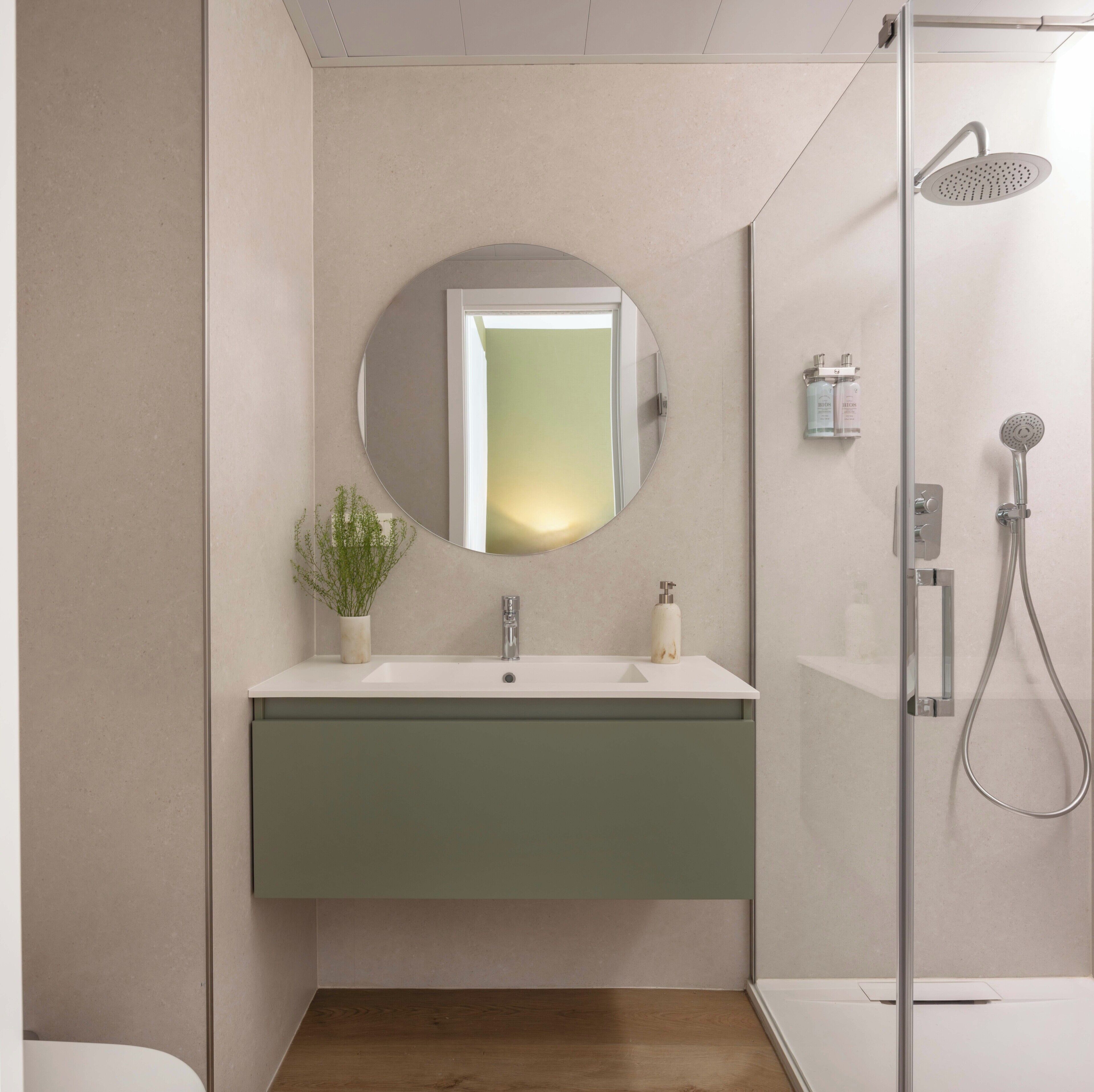 Un baño moderno con un espejo redondo, un lavamanos, una ducha y una planta en maceta.