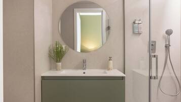 Un baño moderno con un espejo redondo, un lavamanos, una ducha y una planta en maceta.