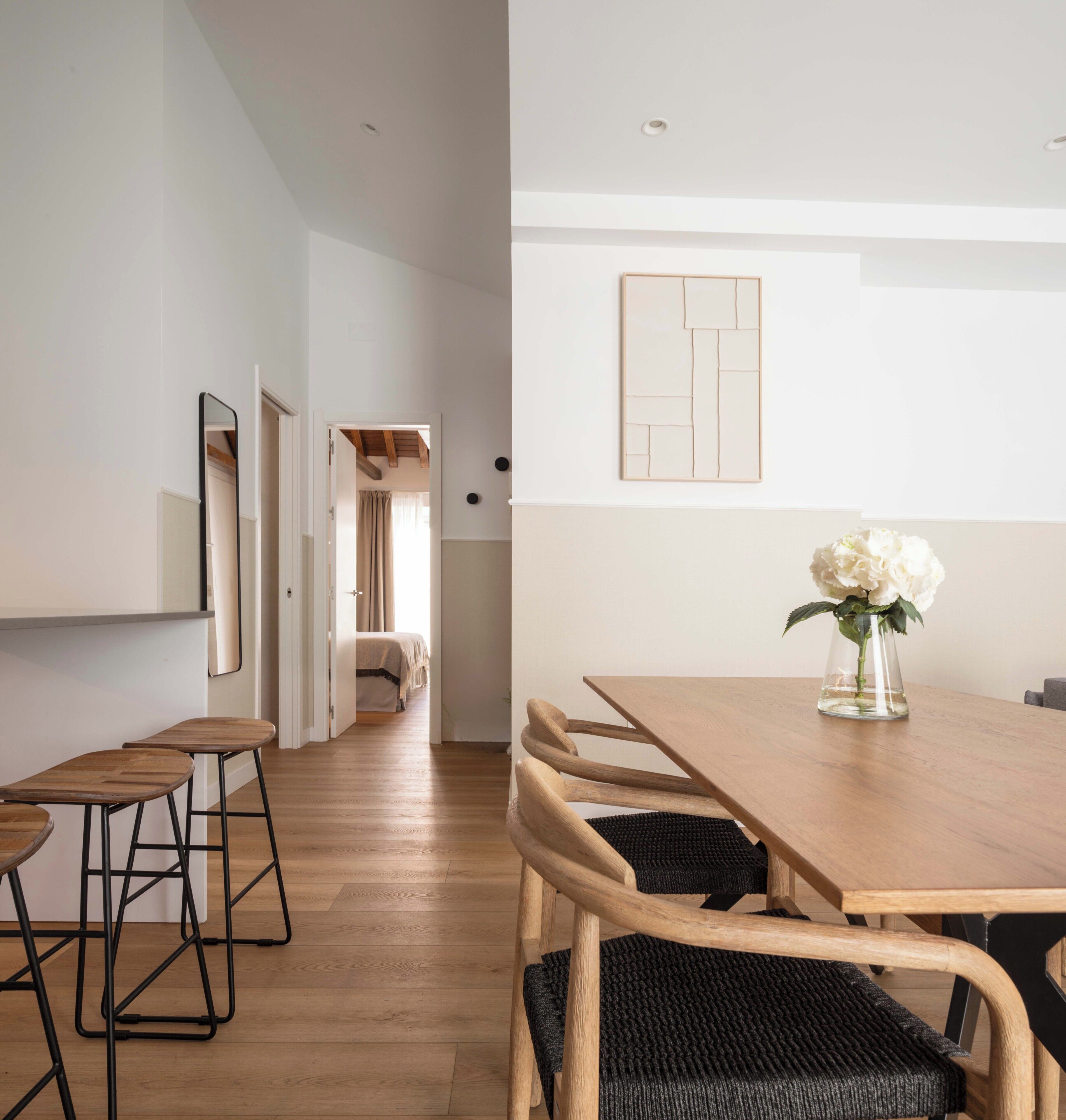 Un espace de repas moderne avec une table et des chaises en bois, un vase rempli de fleurs et un couloir menant à une chambre.