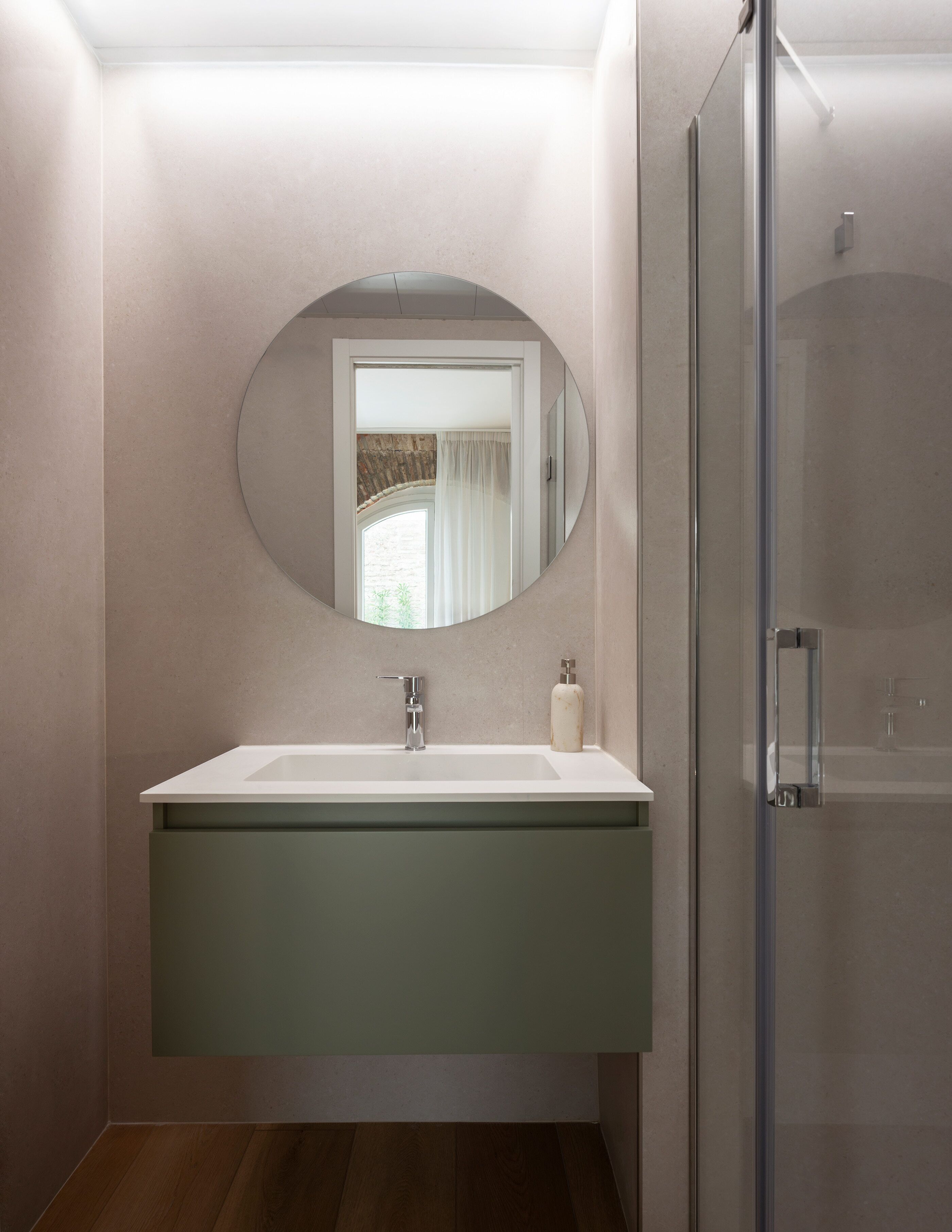 A bathroom with a large mirror, a sink, a glass shower enclosure, and a wooden floor.