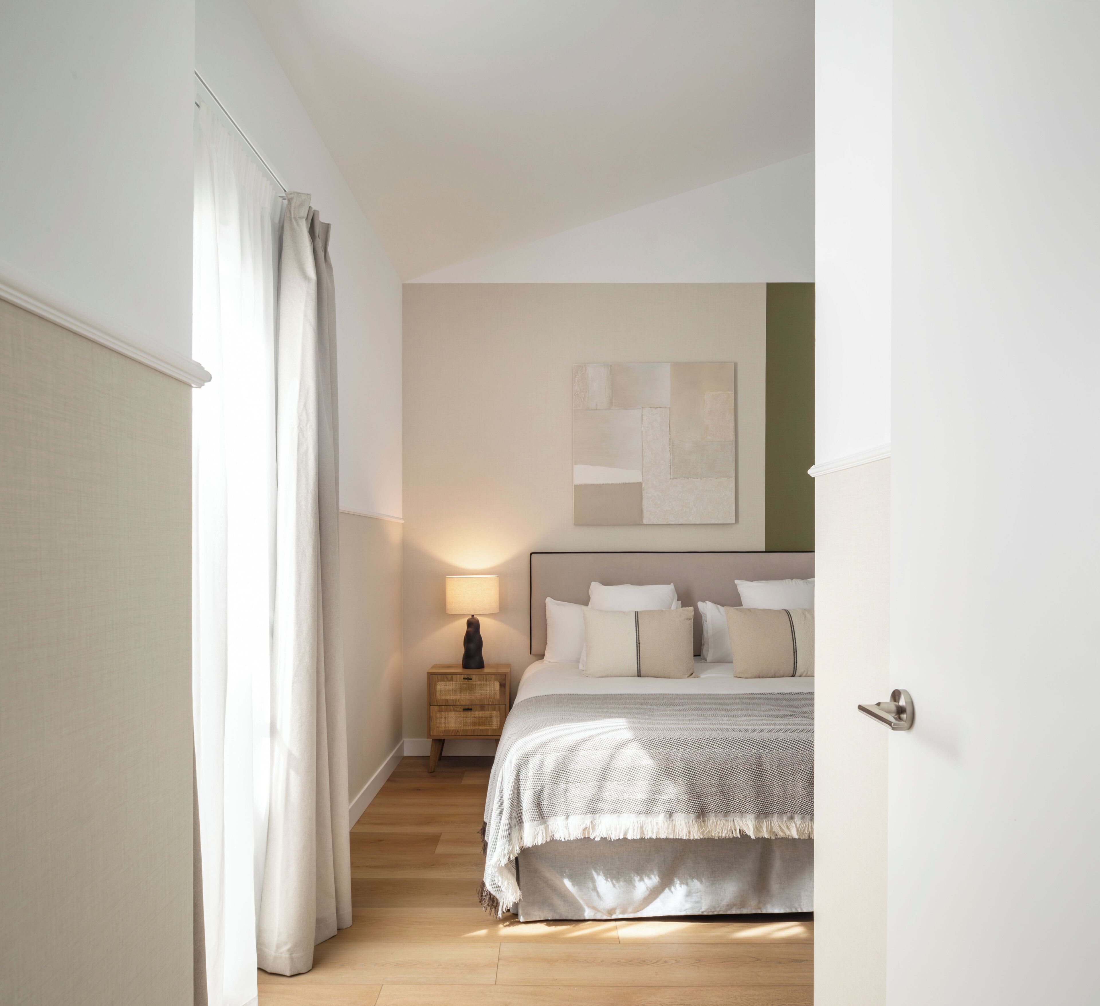 Un dormitorio con cama, mesita de noche, lámpara y un cuadro abstracto en la pared.