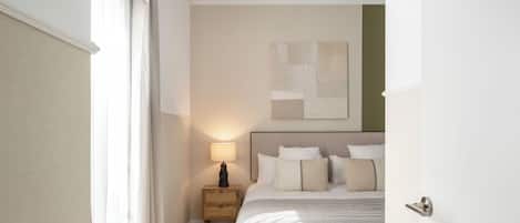 Un dormitorio con cama, mesita de noche, lámpara y un cuadro abstracto en la pared.