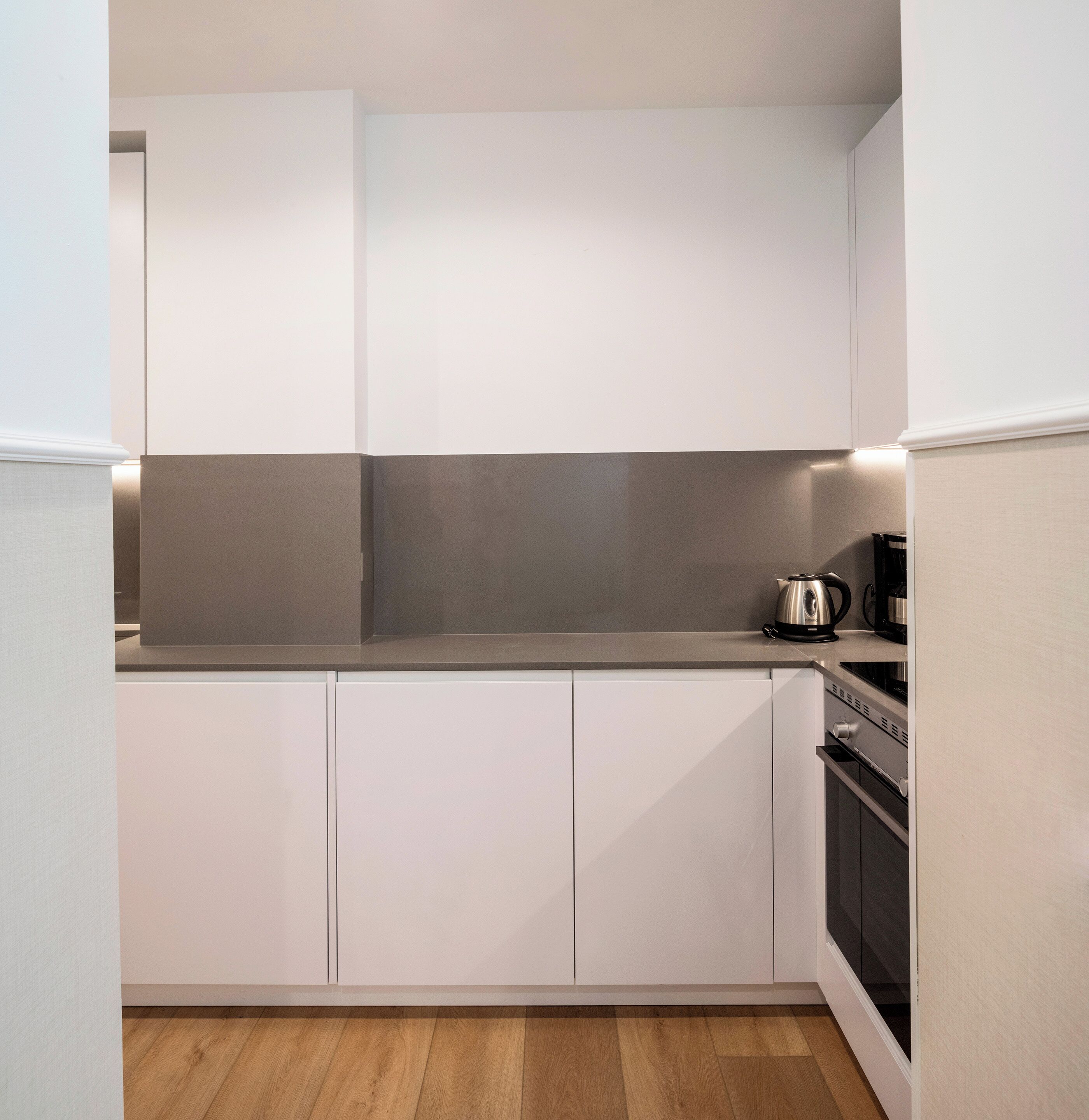 Una cocina compacta con muebles blancos, una encimera gris y un hervidor de acero inoxidable.