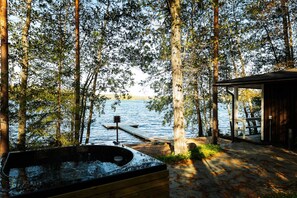 A wooden deck with a hot tub, a dock extending into a lake, and a covered area with a view of the water.