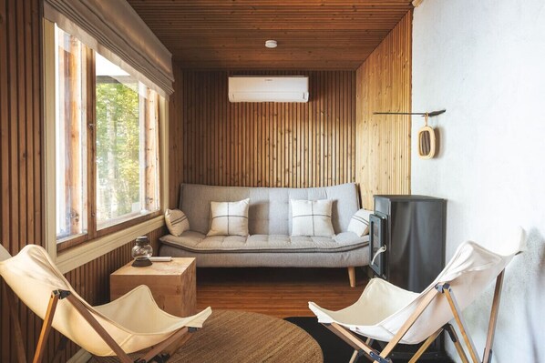 A cozy room with a wooden ceiling, a sofa with cushions, a small table, and two chairs.