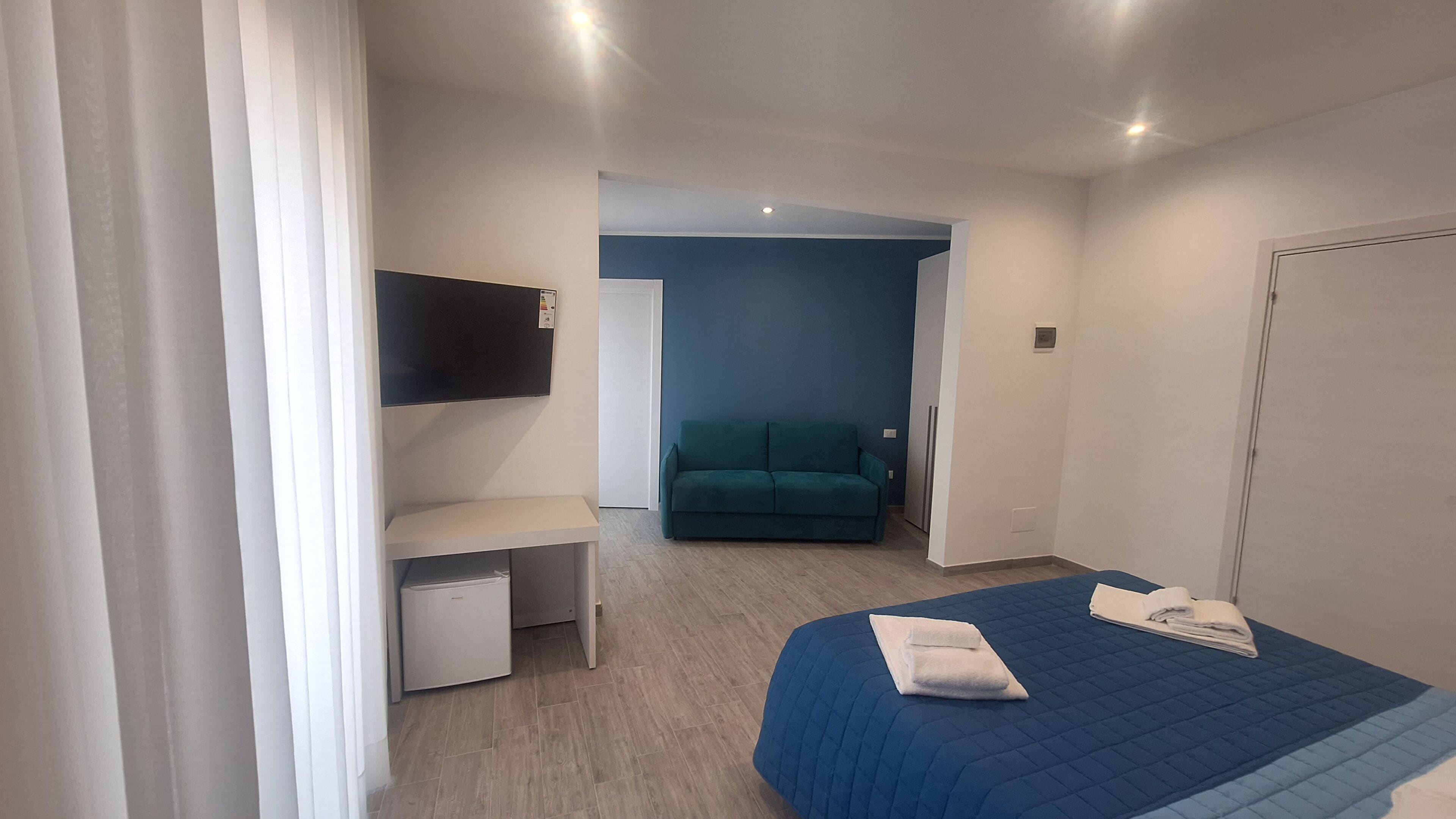 A bedroom with a bed, a desk, a chair, a TV mounted on the wall, and a door.