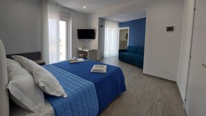 A modern hotel room with a large bed, a desk, a flat-screen TV, and a sofa in the adjacent living area. - Zefiro Rooms (Agrigento)